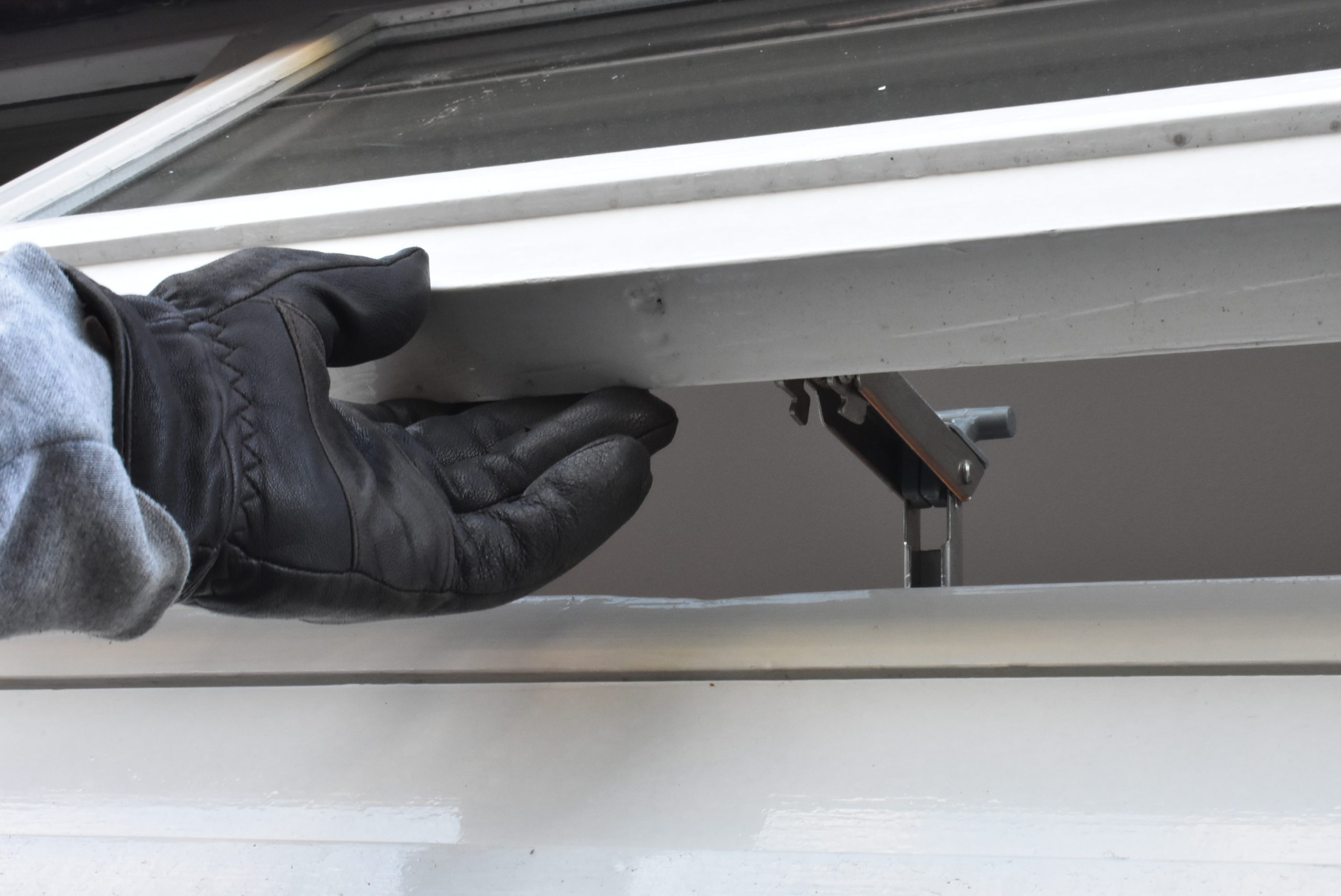 Hand met leren handschoen die probeert een kiepraam te openen om zo het huis binnen te sluipen. Ter illustratie van dossier over Woninginbraak van het CCV en Politiekeurmerk Veilig Wonen/PKVW.