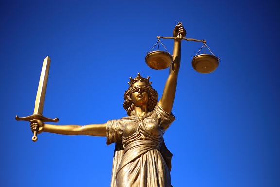 beeld van vrouwe justitia tegen een blauwe achtergrond