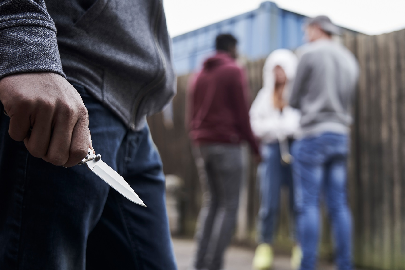 jonge man met mes in hand. Op de achtergrond staat en groepje jongeren bij elkaar.
