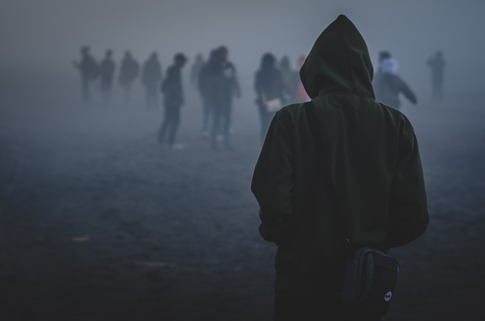 Beeld van rellen. Jongere in hoodie loopt in het donker naar andere jongeren toe.