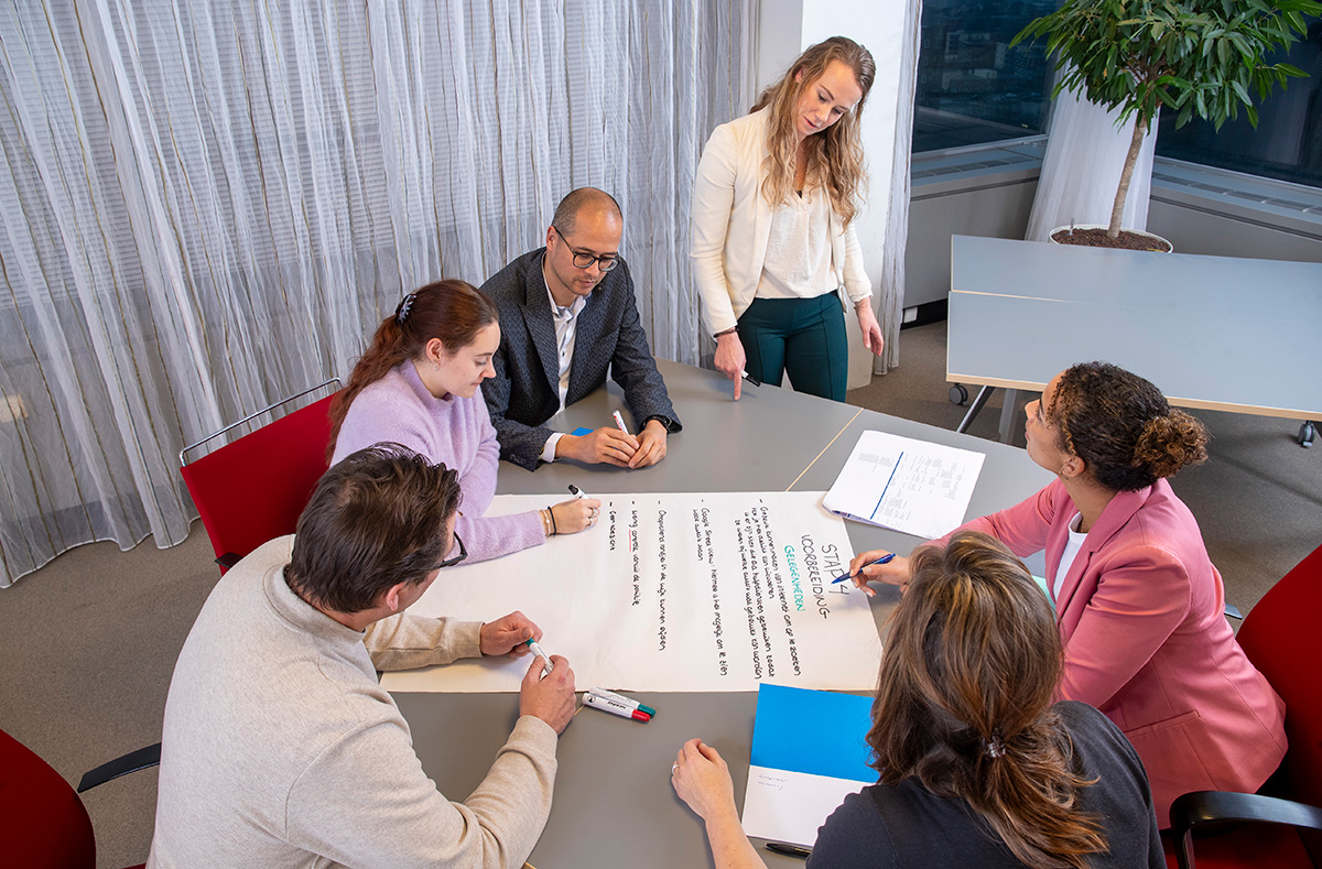 Medewerkers van het CCV in overleg aan een tafel. Op de tafel ligt een vel papier met informatie over de barrièremodellen. Met behulp van de barrièremodellen van het CCV kun je bepalen welke barrières jij en je ketenpartners kunnen opwerpen tegen criminele activiteiten.