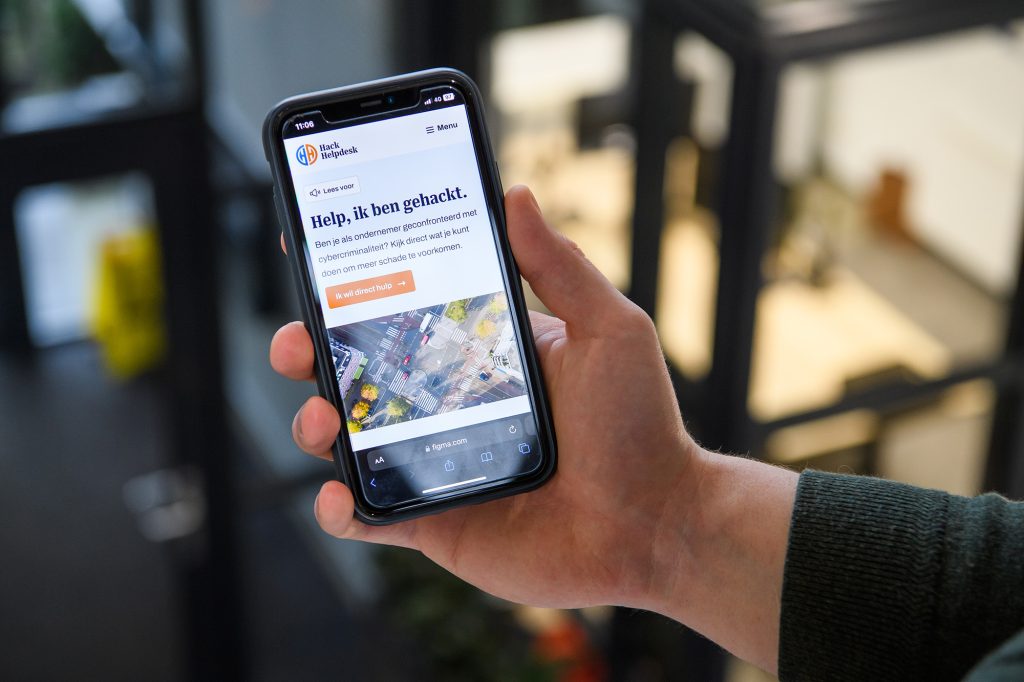 Hand houdt mobiele telefoon vast waarop site van de HackHelpdesk is te zien.