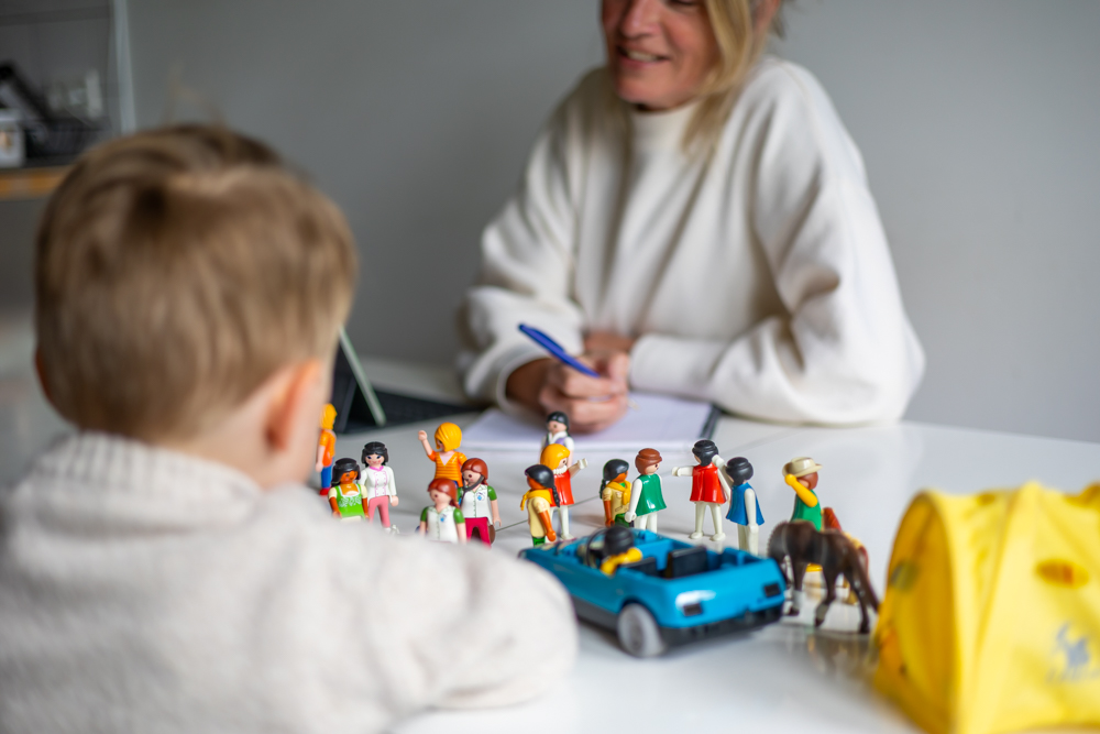 Kind zit aan tafel bij therapeut en vertelt aan de hand van playmobil poppetjes uit wat er is gebeurd.